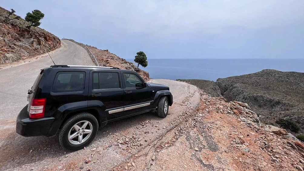Ein schwarzer SUV auf einer kurvenreichen Bergstraße mit felsigem Untergrund und Blick auf das Meer in der Ferne. 3
