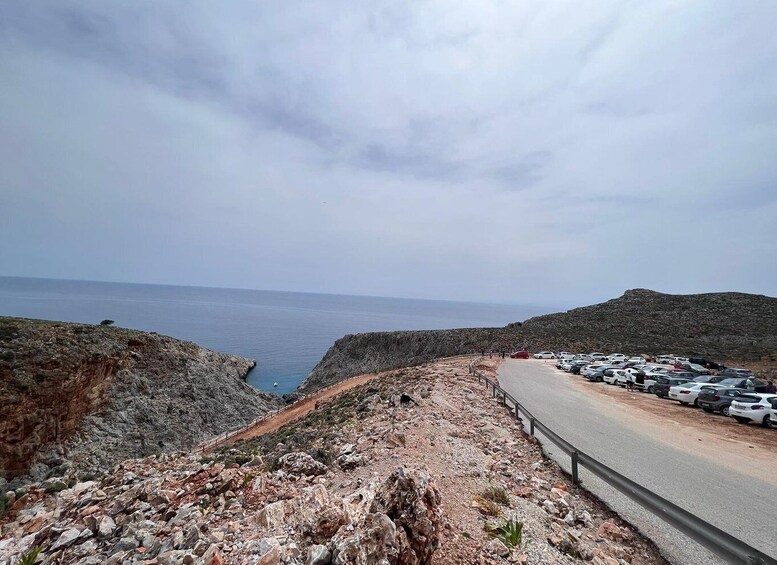 Eine Küstenstraße mit geparkten Autos, felsigem Gelände und dem Meer im Hintergrund. 2