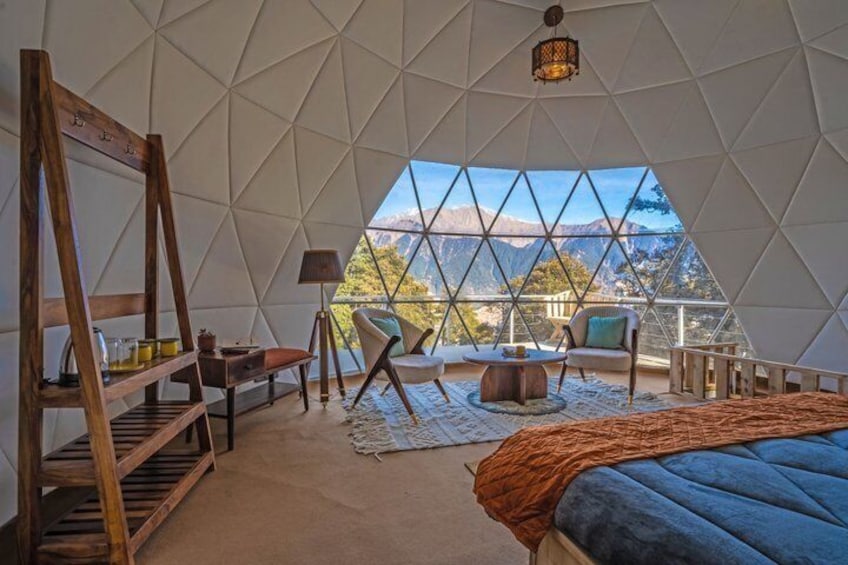 A geodesic dome room with a bed, a wooden ladder, a table, and a chair. 3