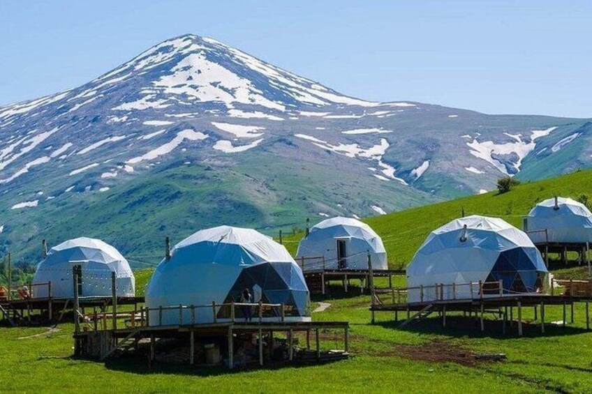 A mountain with snow-capped peaks, several dome-shaped structures, and a grassy foreground. 2