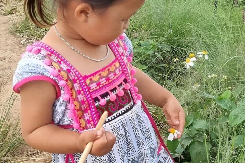 A child in a patterned dress holding a flower. 5