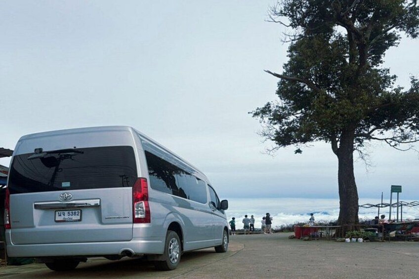 A silver van parked near a tree and a body of water. 3