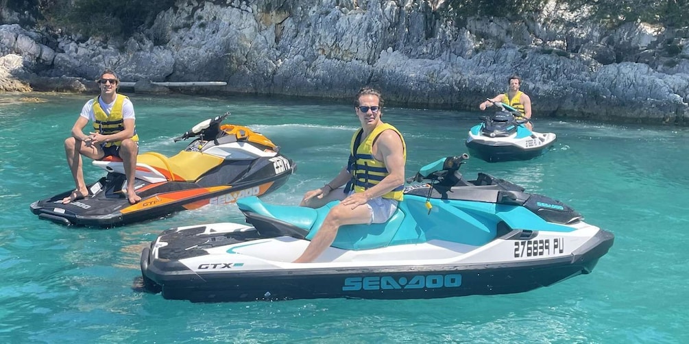 Three people on jet skis in a clear blue body of water with rocky cliffs in the background. 4