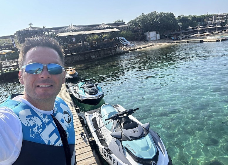 A man on a jet ski docked at a pier with clear water and a beach in the background. 2