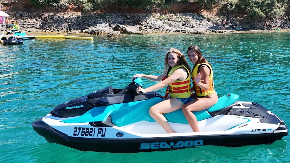 Two people on a Sea-Doo GTX jet ski on a calm lake with clear blue water and rocky shores in the background. 5