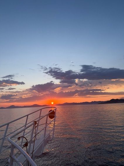 A sunset over a calm sea with a boat's railing in the foreground. 4