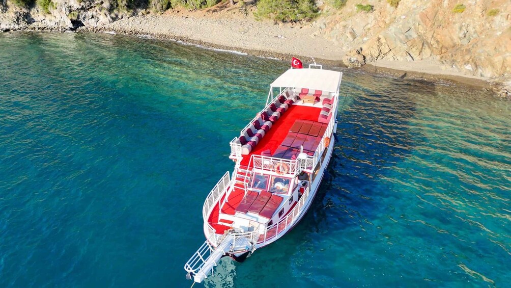 A ferry with red seating, docked at a rocky shoreline. 3