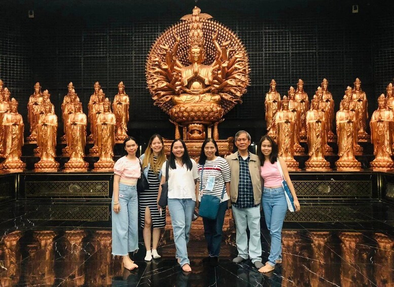 A group of people standing in front of a large golden Buddha statue surrounded by smaller statues. 2