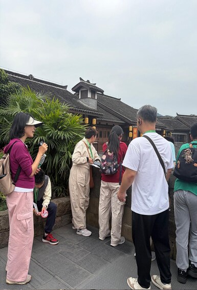 Tourists standing by a traditional building with tiled roofs and a stone wall. 4
