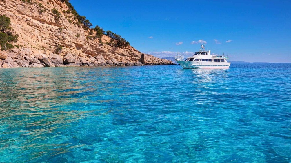 A boat on clear turquoise waters near a rocky coastline. 2