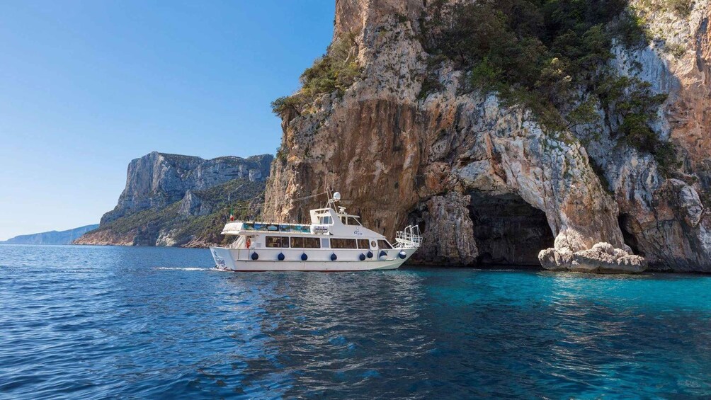 A boat navigating near a rocky coastline with cliffs and clear blue waters. 3