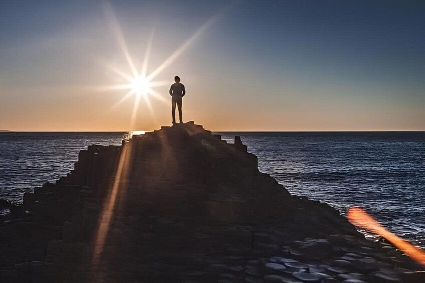 A person standing on a rocky outcrop with the sun setting in the background. 3