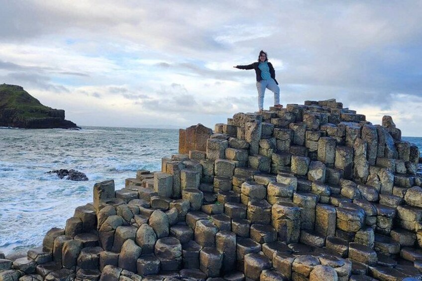 A person standing on a stone structure by the sea with waves crashing below. 1