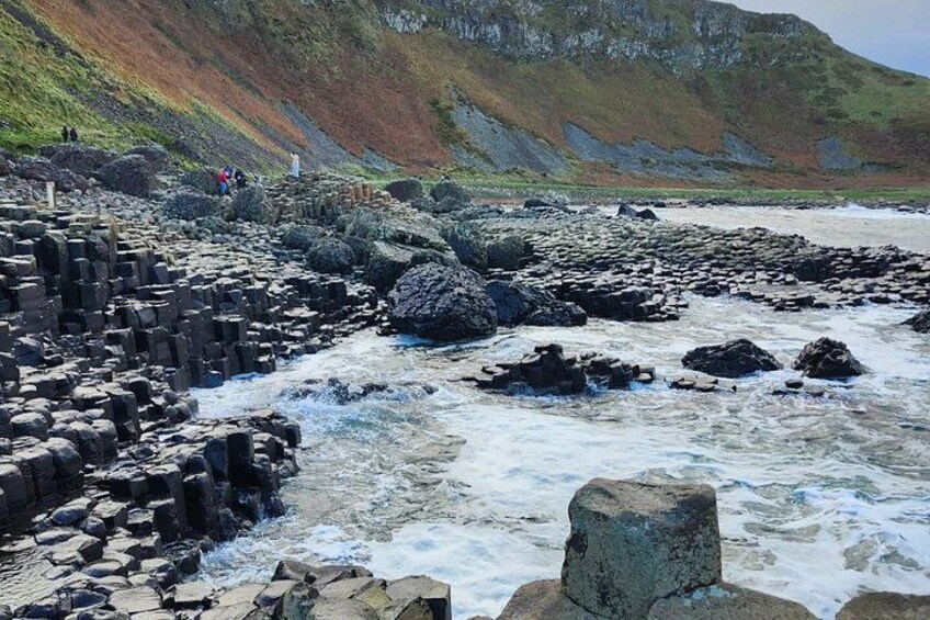 A rocky coastline with waves crashing against large boulders and a distant hill. 2
