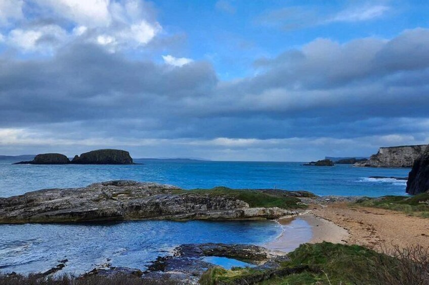 A coastal landscape with rocky outcrops, a sandy beach, and calm blue waters. 3