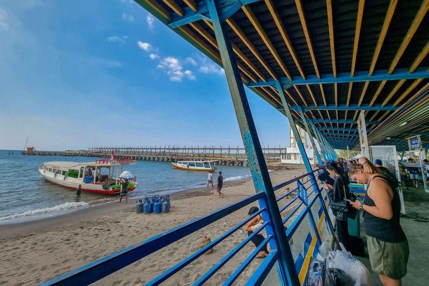 A beach with a pier in the background, a boat on the sand, and people near the water. 1