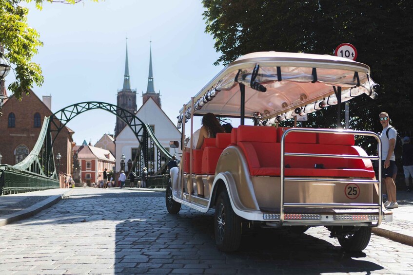 A vintage car parked on a cobblestone street with a bridge and church in the background. 3