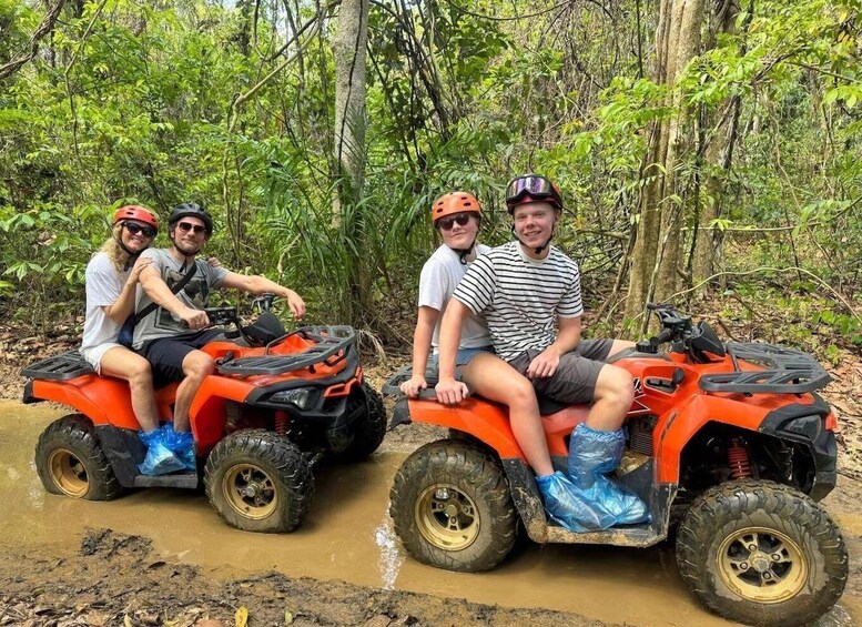 Four people on an ATV in a muddy forest. 4