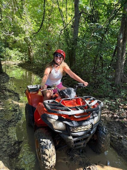 A person riding an ATV through a muddy forest path. 2