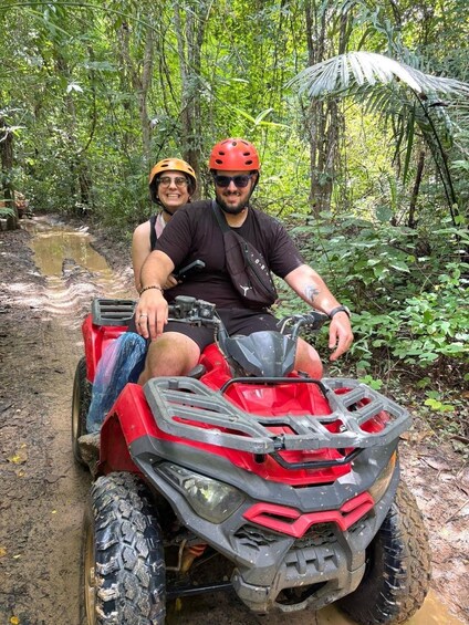Two people on a red ATV in a forested area with muddy paths. 5