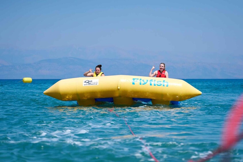 Two people on a yellow inflatable boat with 'Flyfish' written on it, floating on water with mountains in the background. 2