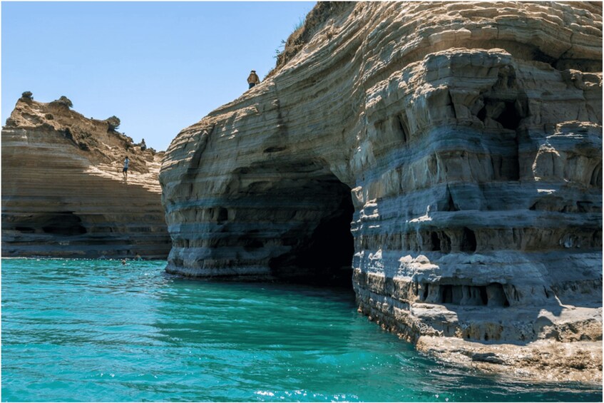 A coastal rock formation with layered strata and a cave entrance. 3
