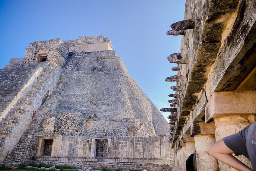 An ancient pyramid with a staircase leading to the top, a stone building with columns, and a clear blue sky. 5