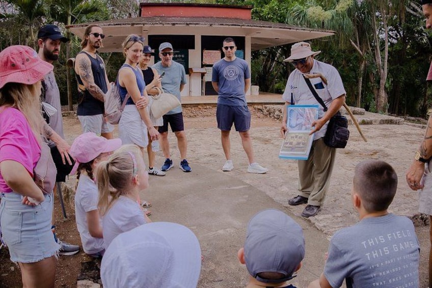 A group of people gathered around a guide holding a map, standing in an outdoor setting with a building in the background. 3