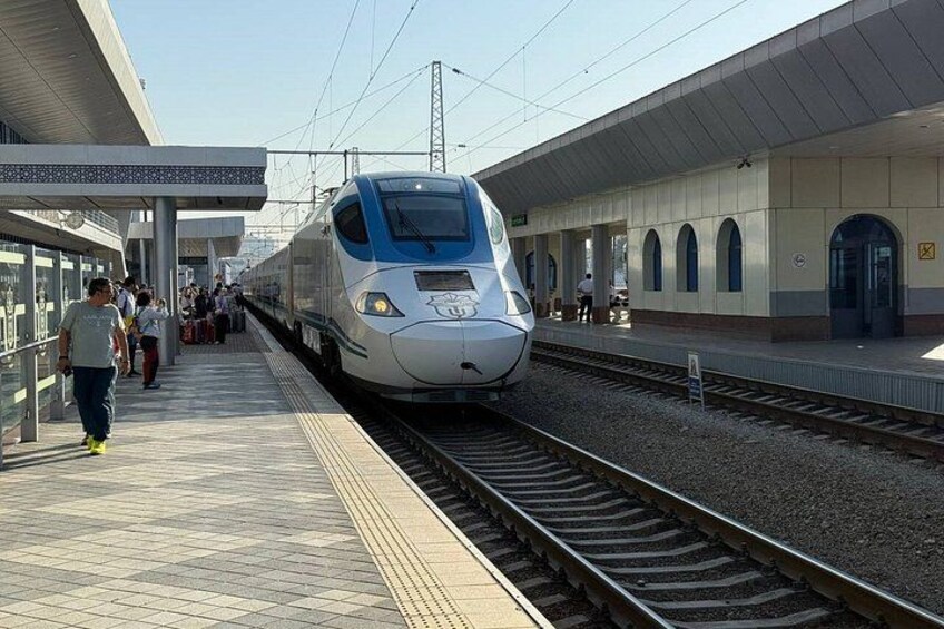 A modern train at a station platform with passengers waiting. 5