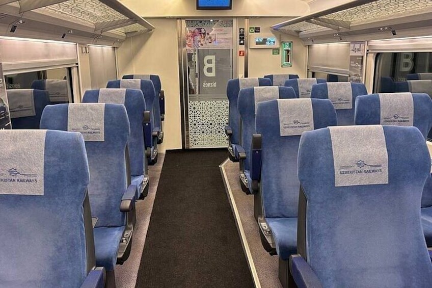 A train interior with rows of blue seats, a central aisle, and overhead compartments. 4