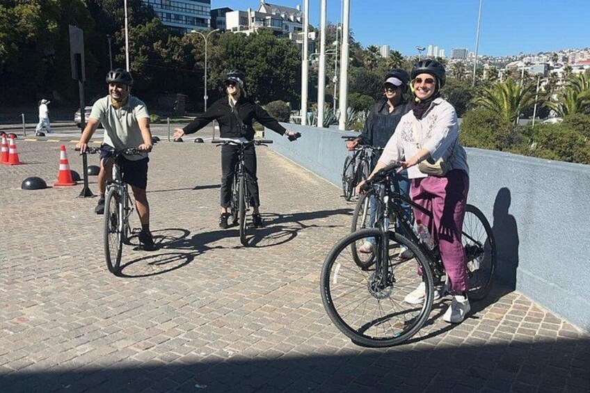 A group of people on bicycles on a paved path with traffic cones and a railing. 5