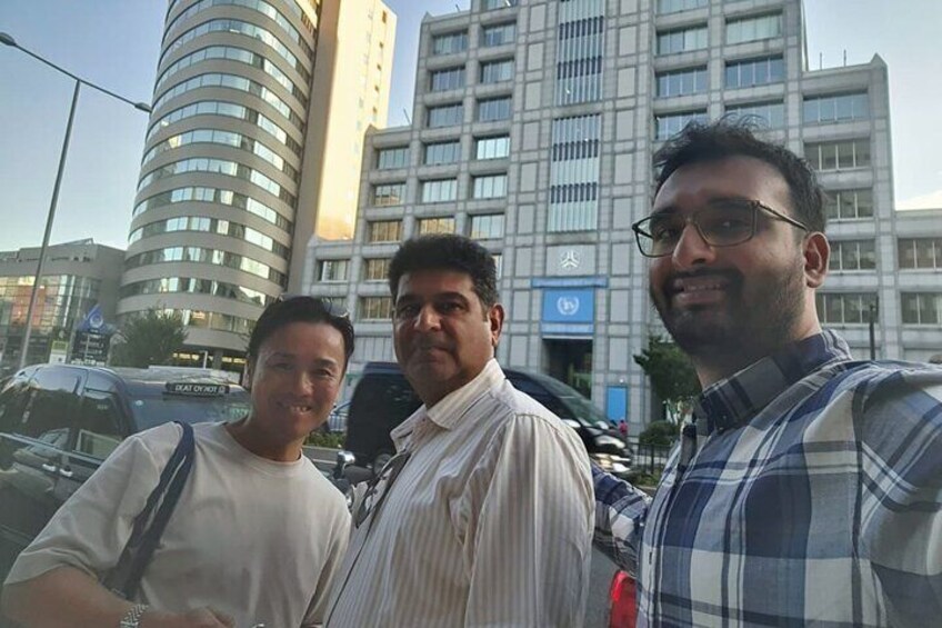 Three men standing in front of a modern building with a curved facade and a sign with a globe symbol. 5