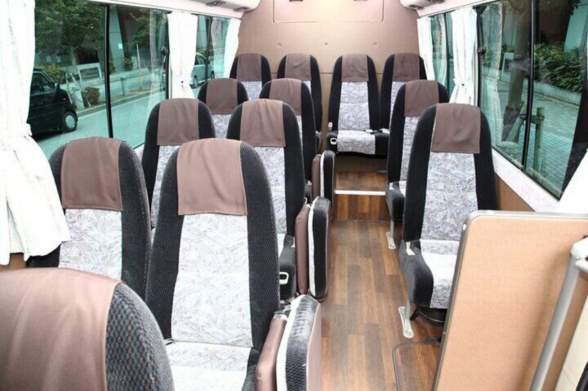 A bus interior with rows of seats, a wooden floor, and a window on the right side. 2