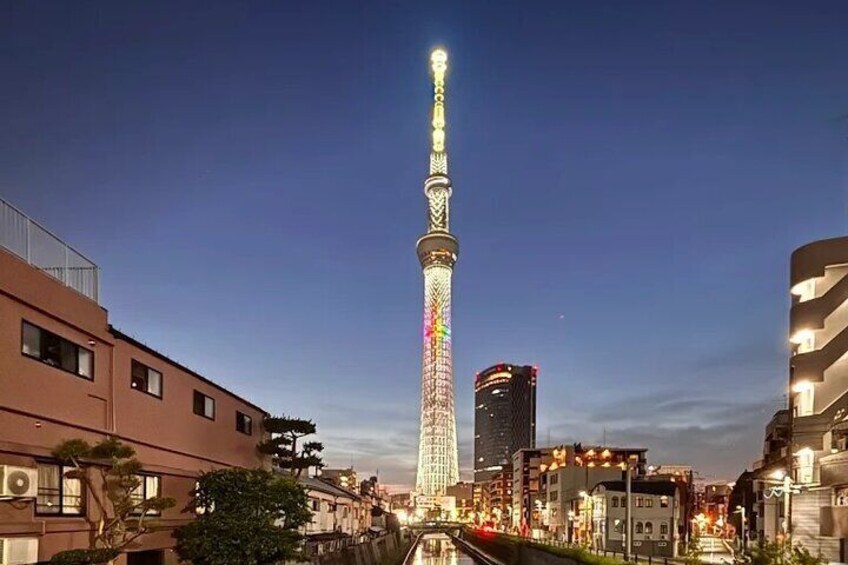 A brightly lit tower with a spiral design, surrounded by urban buildings and a clear sky. 1