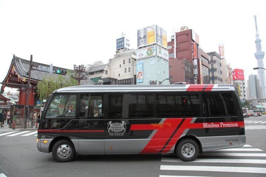 A Minibus Premium with 'OLITEC' branding, driving on a city street with traditional architecture and a modern tower in the background. 4