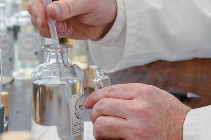 A person handling a glass bottle with a white label, using a dropper to extract a liquid. 4