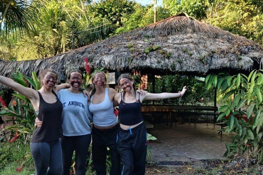 Four people standing in front of a thatched-roof structure surrounded by greenery. 4