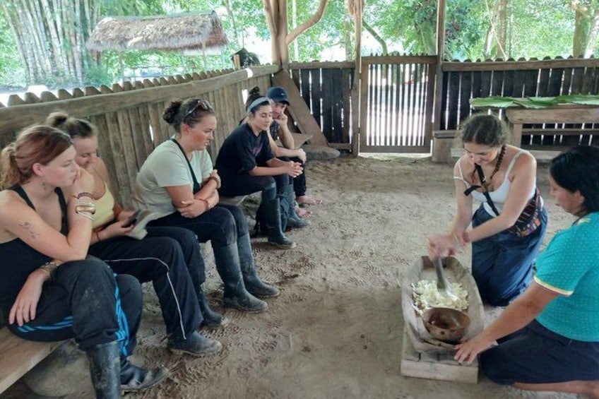 A group of people sitting on benches under a wooden structure, with one person mixing something in a container. 5