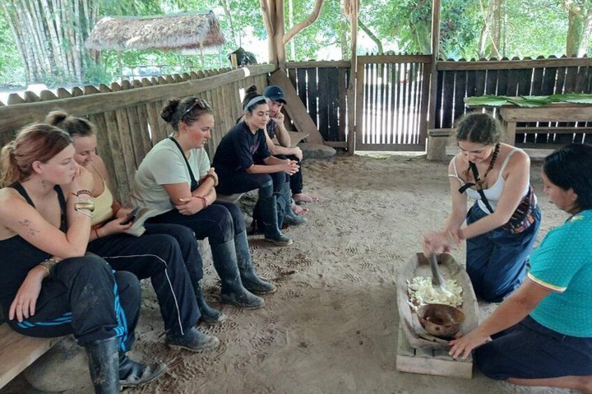 A group of people sitting on benches in a rustic outdoor setting, with one person mixing ingredients in a large bowl. 5