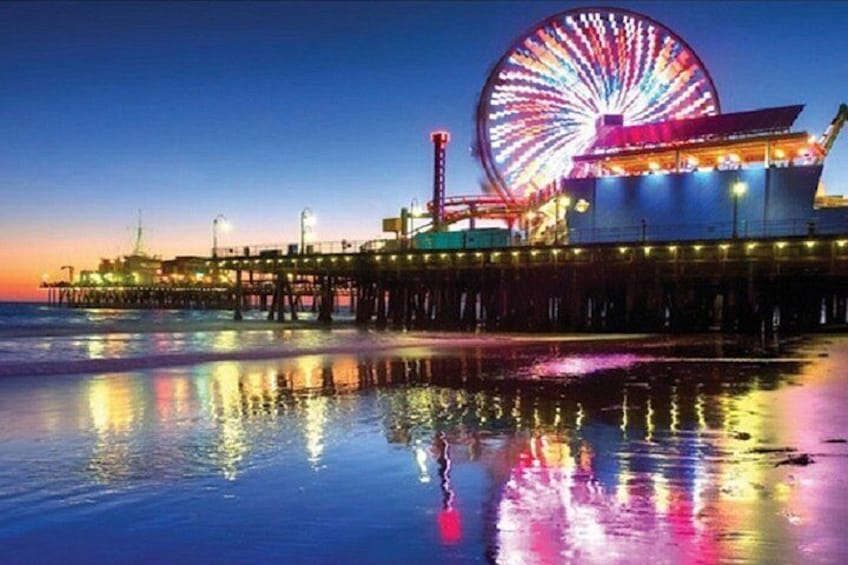 A pier with a large Ferris wheel, a body of water reflecting lights, and a sunset sky. 5