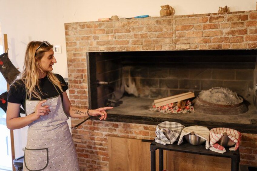 A person in an apron pointing at a brick fireplace with a pizza stone and pizza peel on the counter. 3