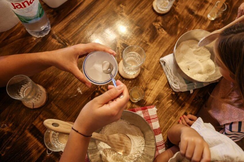 A person holding a measuring cup over a bowl of flour, with a bottle of water and a glass on the table. 4