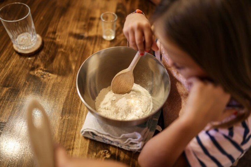 A child mixing ingredients in a metal bowl on a wooden table. 5