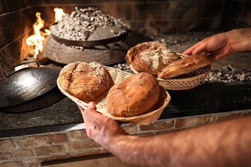 A person holding a basket with bread near a wood-fired oven. 4