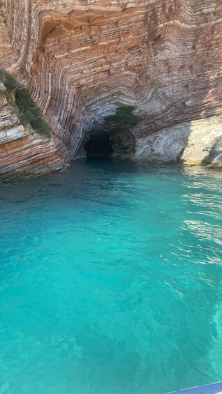 A natural rock formation with a cave entrance and clear turquoise water. 1