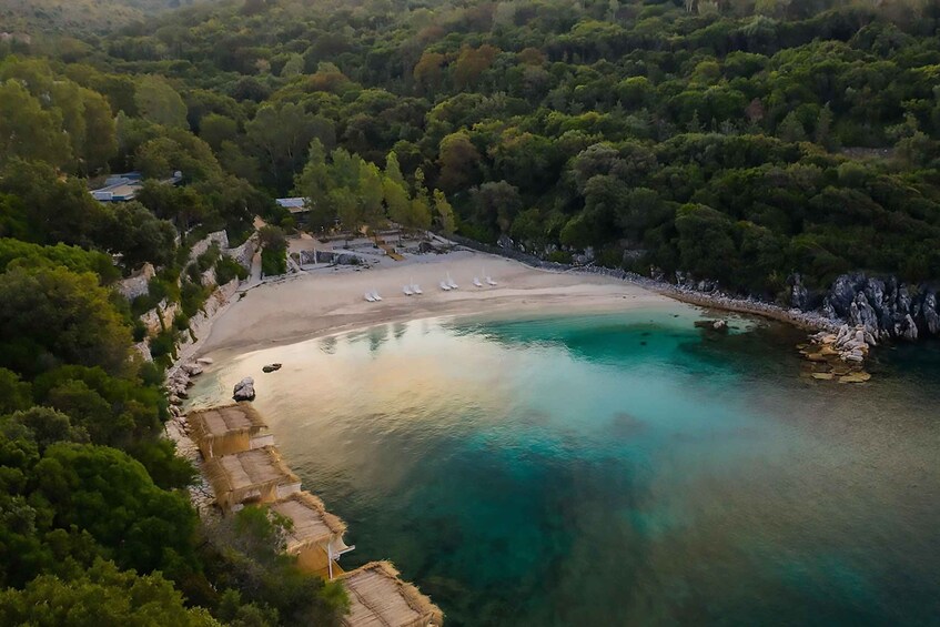 A coastal landscape with a sandy beach, clear turquoise waters, and dense green forest. 5