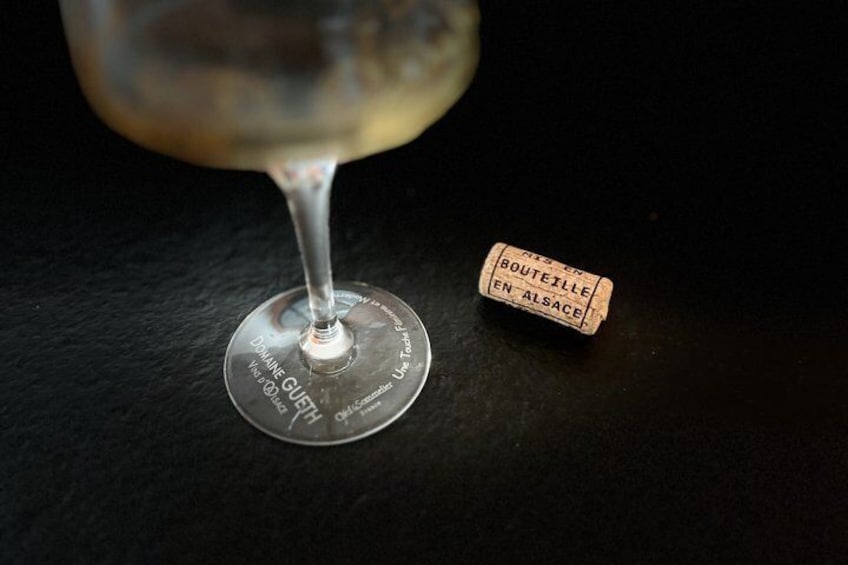 A wine glass with a label 'Domaine GLUET' and a small cork with 'BOUTEILLE EN ALSACE' text. 2