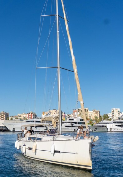 A sailboat with passengers on a calm sea, with buildings in the background. 1