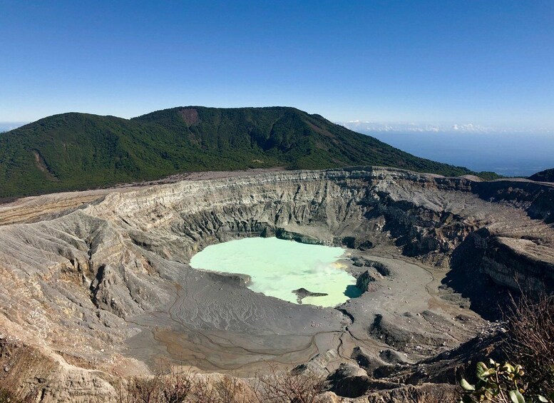 A volcanic crater with a turquoise lake surrounded by rugged terrain and forested hills. 3