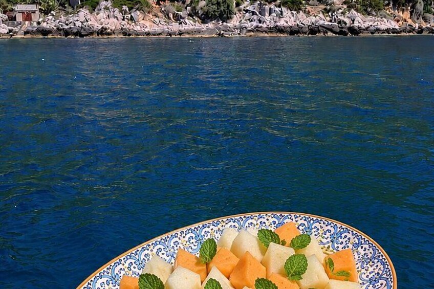 A bowl of fruit on a boat with a rocky shoreline in the background. 5